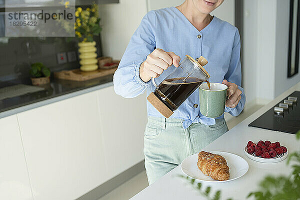 Frau gießt Kaffee in Tasse mit Croissant auf die Theke zu Hause