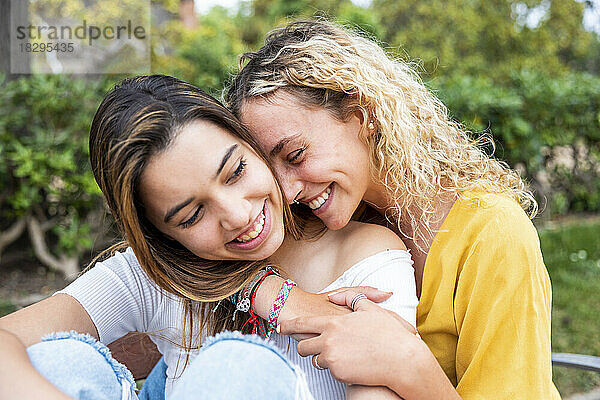 Smiling young woman with blond hair embracing girlfriend in park