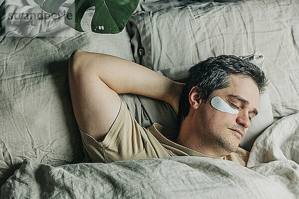 Man with under eye patches sleeping in bedroom