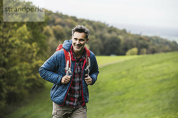 Lächelnder Mann mit Rucksack  der auf Gras steht