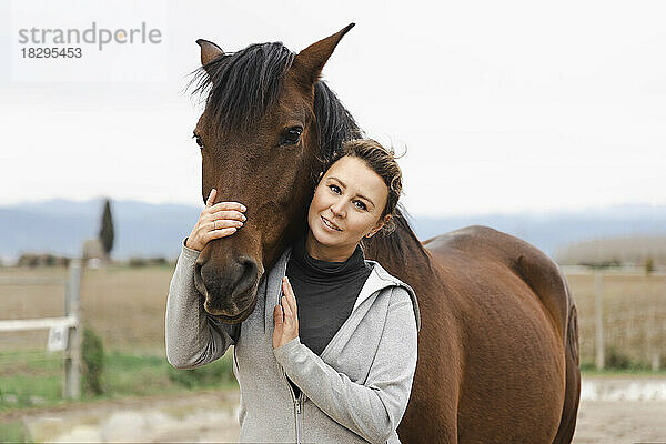 Lächelnde Frau umarmt braunes Pferd auf der Ranch