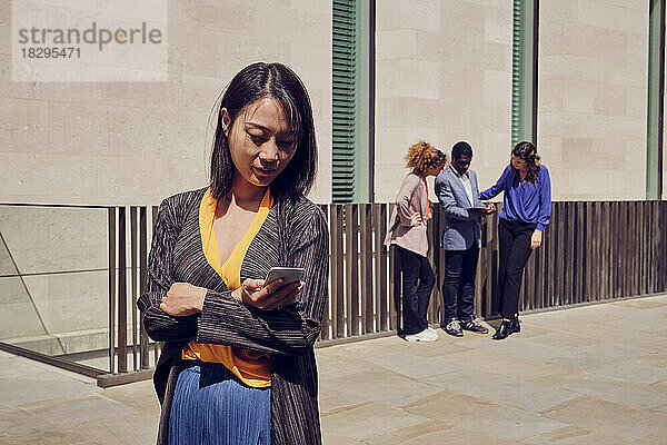 Geschäftsfrau benutzt Smartphone  im Hintergrund stehen Kollegen