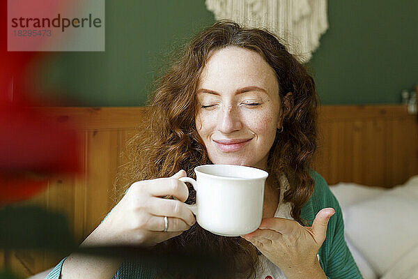 Lächelnde Frau mit geschlossenen Augen  die zu Hause Tee trinkt