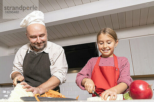 Vater und Tochter tragen Schürzen und bereiten zu Hause in der Küche gesunde Mahlzeiten zu
