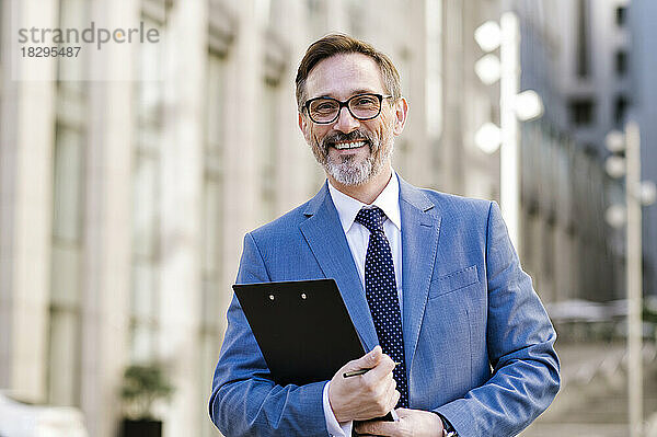 Happy mature businessman holding clipboard outside building