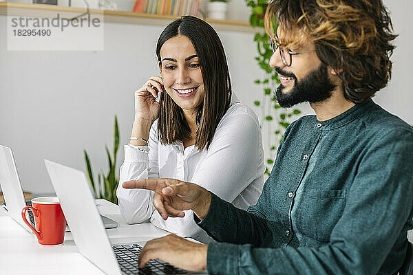 Glückliche Freiberufler diskutieren am Laptop am Schreibtisch im Büro