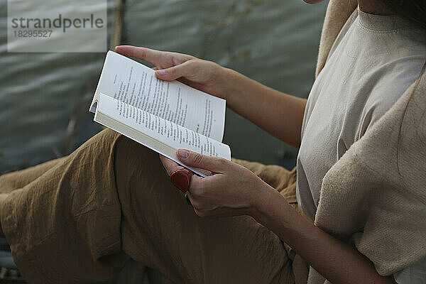 Frau sitzt mit Buch am Fluss