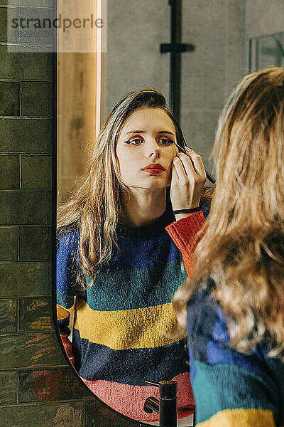 Blond girl doing makeup in front of bathroom mirror