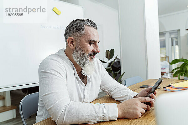 Reifer Geschäftsmann nutzt Smartphone am Schreibtisch im Büro