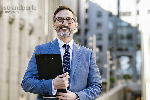 Contemplative mature businessman with clipboard outside building exterior