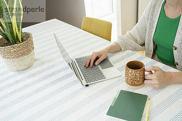 Freiberufler nutzt Laptop mit Teetasse auf dem Schreibtisch im Heimbüro