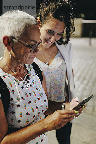 Ältere Frau teilt nachts ihr Smartphone mit einer Freundin