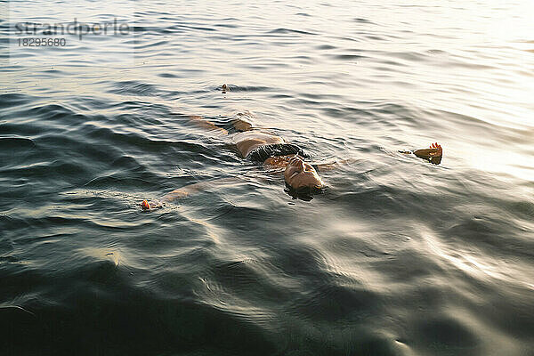 Frau schwimmt bei Sonnenuntergang im Meer