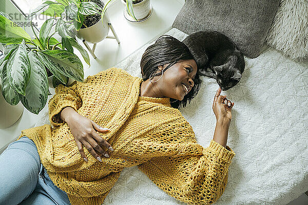 Lächelnde junge Frau liegt mit Katze zu Hause