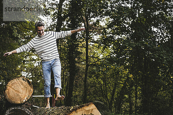 Fröhlicher reifer Mann  der auf einem Baumstamm im Wald spaziert