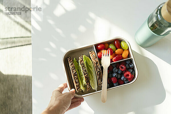 Hand of woman holding lunch box with healthy food on table