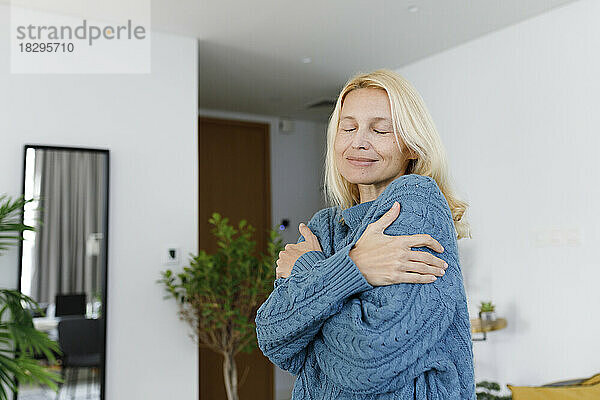 Smiling woman with eyes closed hugging self