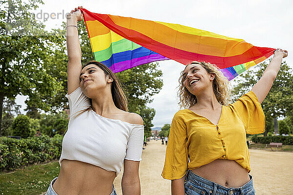 Lesbisches Paar hält Regenbogenfahne im Park