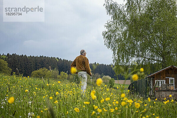 Älterer Mann steht inmitten gelber Blumen auf einer Wiese unter freiem Himmel