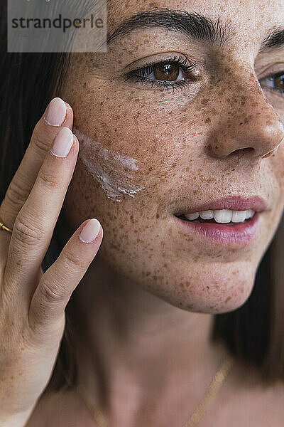 Junge Frau mit Sommersprossen im Gesicht  die Feuchtigkeitscreme auf das Gesicht aufträgt