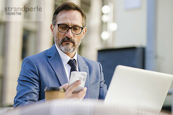 Reifer Geschäftsmann sitzt im Café und benutzt Smartphone