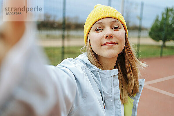 Lächelndes Mädchen mit Strickmütze macht ein Selfie auf dem Spielplatz