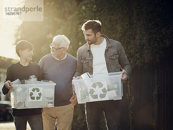 Großvater  Vater und Sohn stehen draußen und tragen Recyclingboxen mit getrenntem Müll