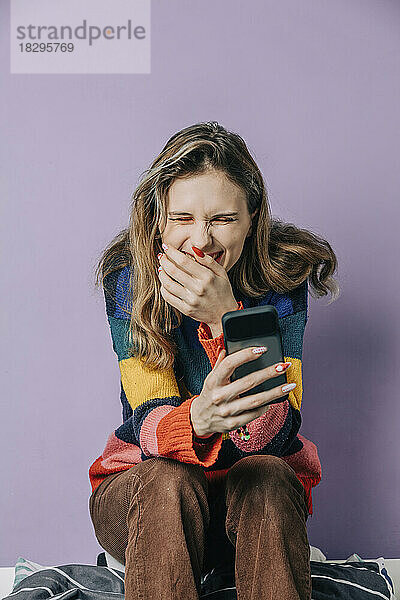 Smiling girl using smart phone sitting against purple background