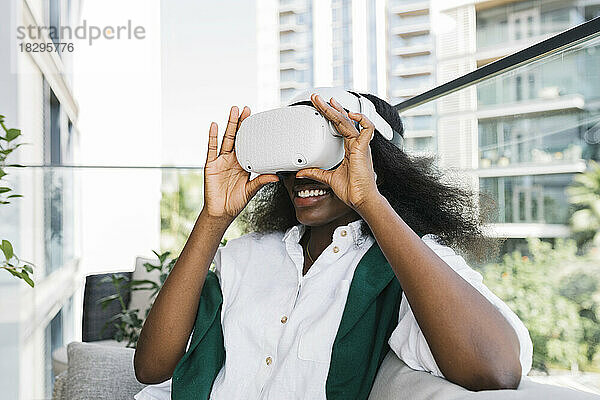 Glückliche Frau mit Virtual-Reality-Simulatoren sitzt auf dem Balkon