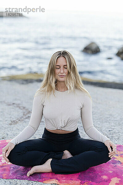 Frau im Lotussitz praktiziert Yoga am Strand