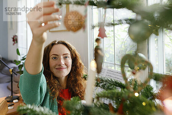 Lächelnde Frau schmückt zu Hause den Weihnachtsbaum