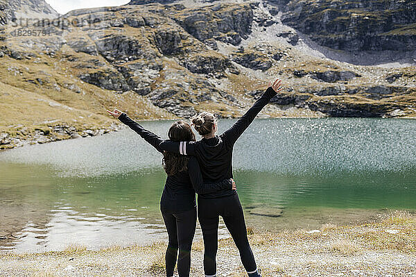 Wanderer umarmen sich und stehen mit erhobenen Armen am See