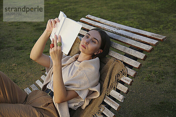 Young woman reading book on deck chair