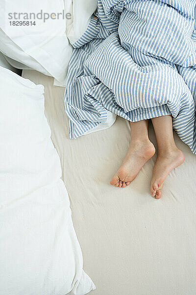 Legs of girl under duvet on bed at home