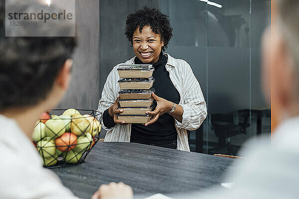 Fröhliche junge Frau mit Lunchboxen steht am Tisch im Büro