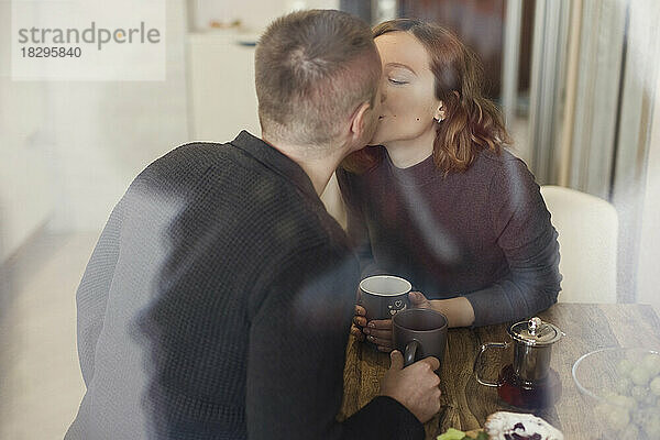 Mann und Frau küssen sich  gesehen durch ein Glasfenster