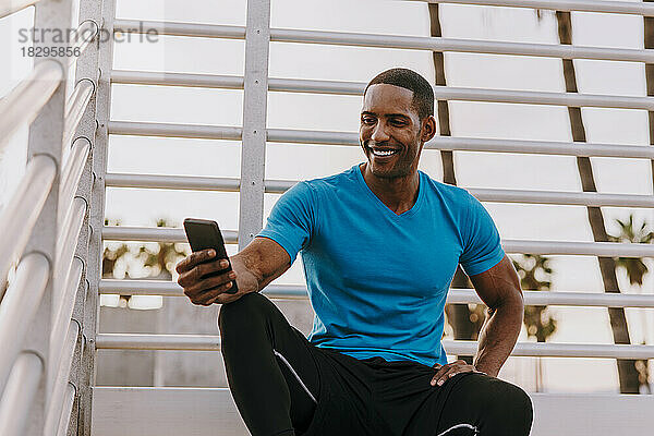 Glücklicher Mann sitzt mit Smartphone vor dem Geländer