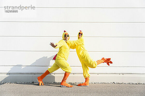 Verspielte Männer und Frauen in Hühnerkostümen amüsieren sich vor der Wand