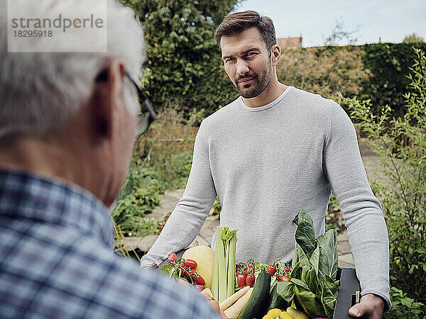 Man delivering a fresh vegetable box to senior man in garden
