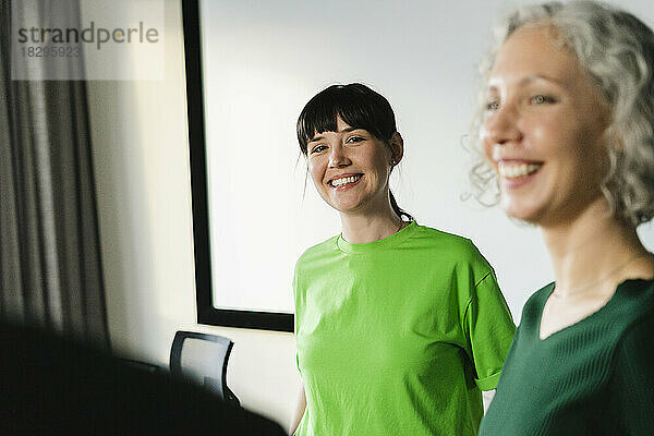 Two happy colleagues in green clothing in office