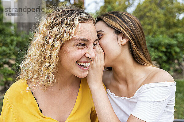 Young woman whispering into friend's ear in park