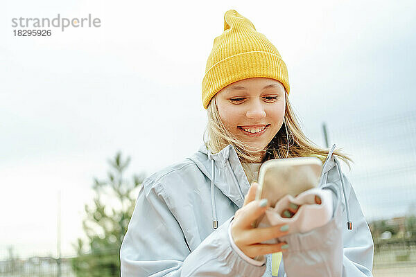 Fröhliches Teenager-Mädchen benutzt Smartphone unter Himmel