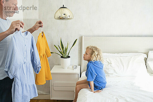 Vater zeigt seiner Tochter  die zu Hause im Bett sitzt  Kleider