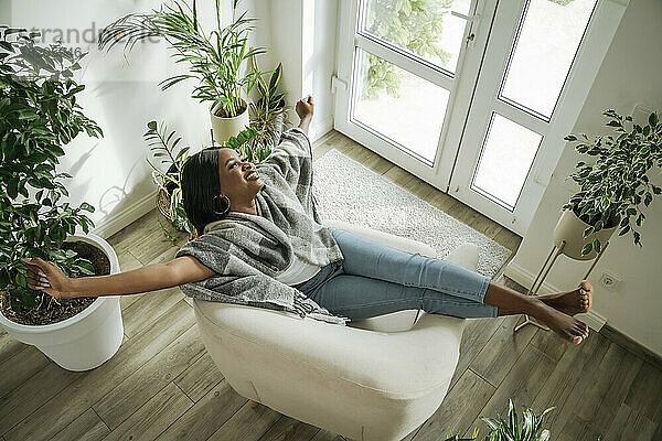 Happy woman stretching arms relaxing in armchair at home