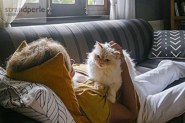 Ältere Frau mit Katze kuschelt zu Hause auf dem Sofa