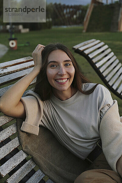 Glückliche junge Frau sitzt auf Liegestuhl im Park