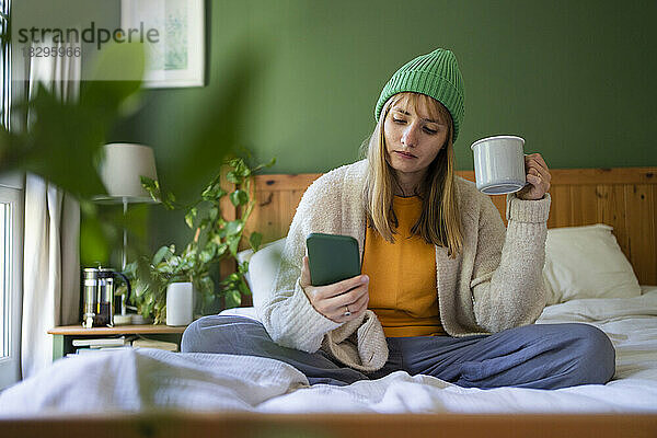 Frau mit Teetasse nutzt Smartphone zu Hause