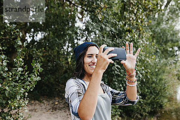 Lächelnde junge Frau  die im Park mit dem Smartphone auf Fotos klickt