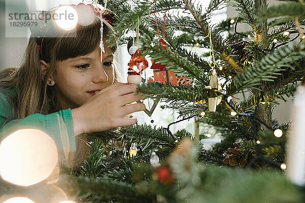 Mädchen schmückt Weihnachtsbaum zu Hause