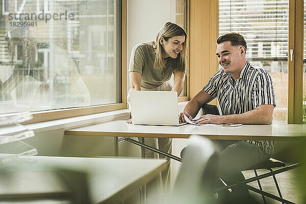 Lächelnde Geschäftsfrau und Geschäftsmann diskutieren am Laptop im Büro